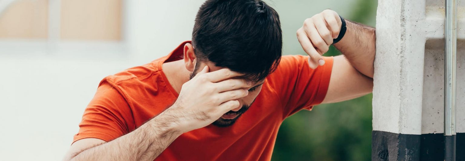 Man Experiencing Dizzy Spell man resting elbow against wall and holing head to stop dizziness