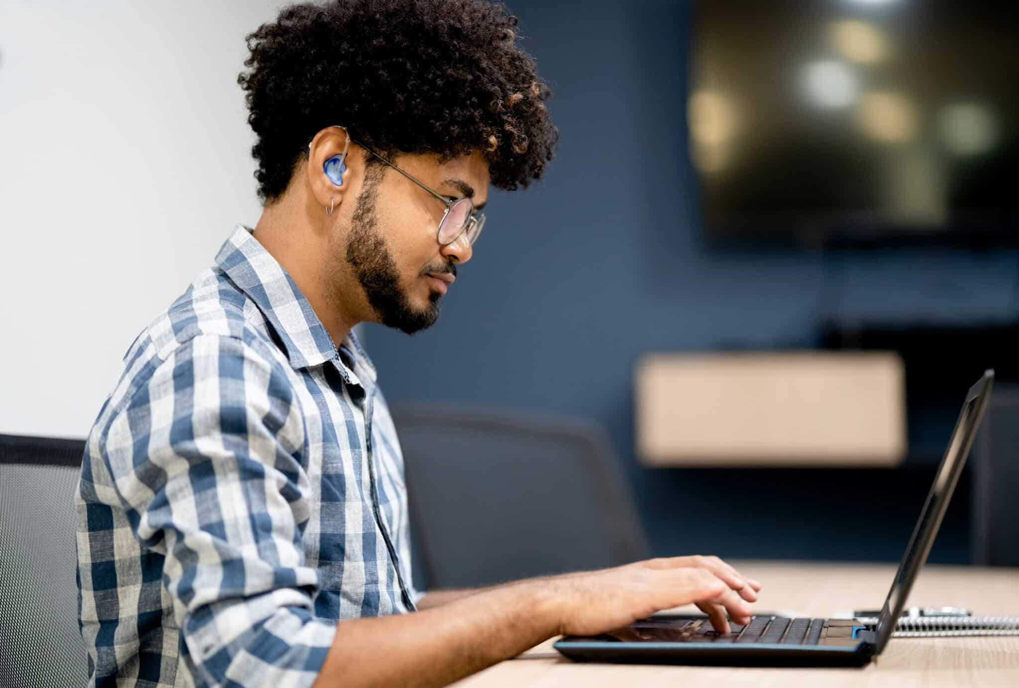 Man with a hearing aid working on laptop at office Side view of man with a hearing aid working on laptop at office