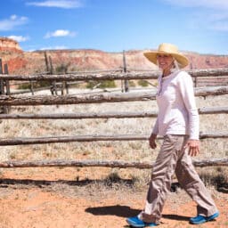 Woman on a ranch in New Mexico walking outside exposed to the dust and the heat. She wears a wide-brimmed hat to protect her hearing devices.