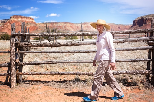 Woman on a ranch in New Mexico walking outside exposed to the dust and the heat. She wears a wide-brimmed hat to protect her hearing devices. 